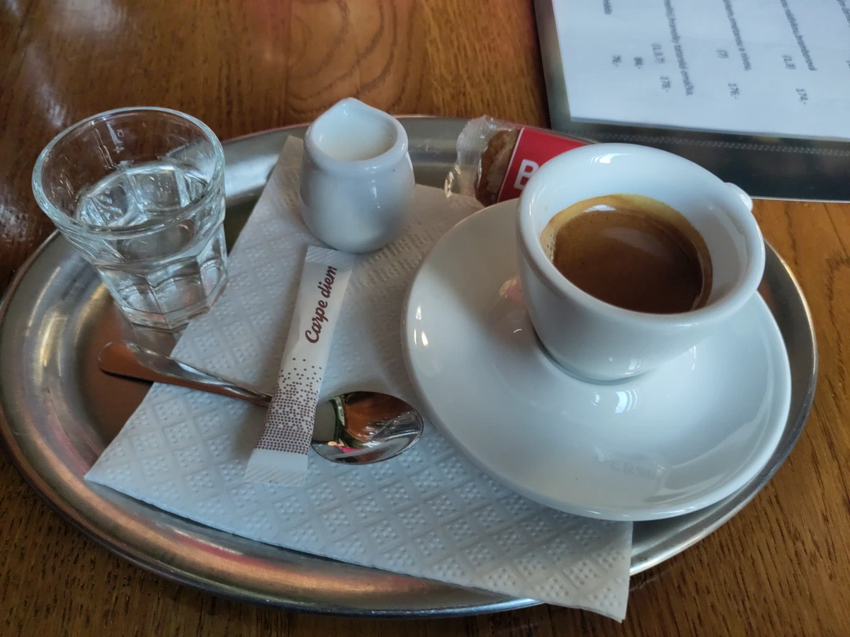 Espresso auf einem Metalltablett, daneben ein Glas Wasser und ein Milchkännchen