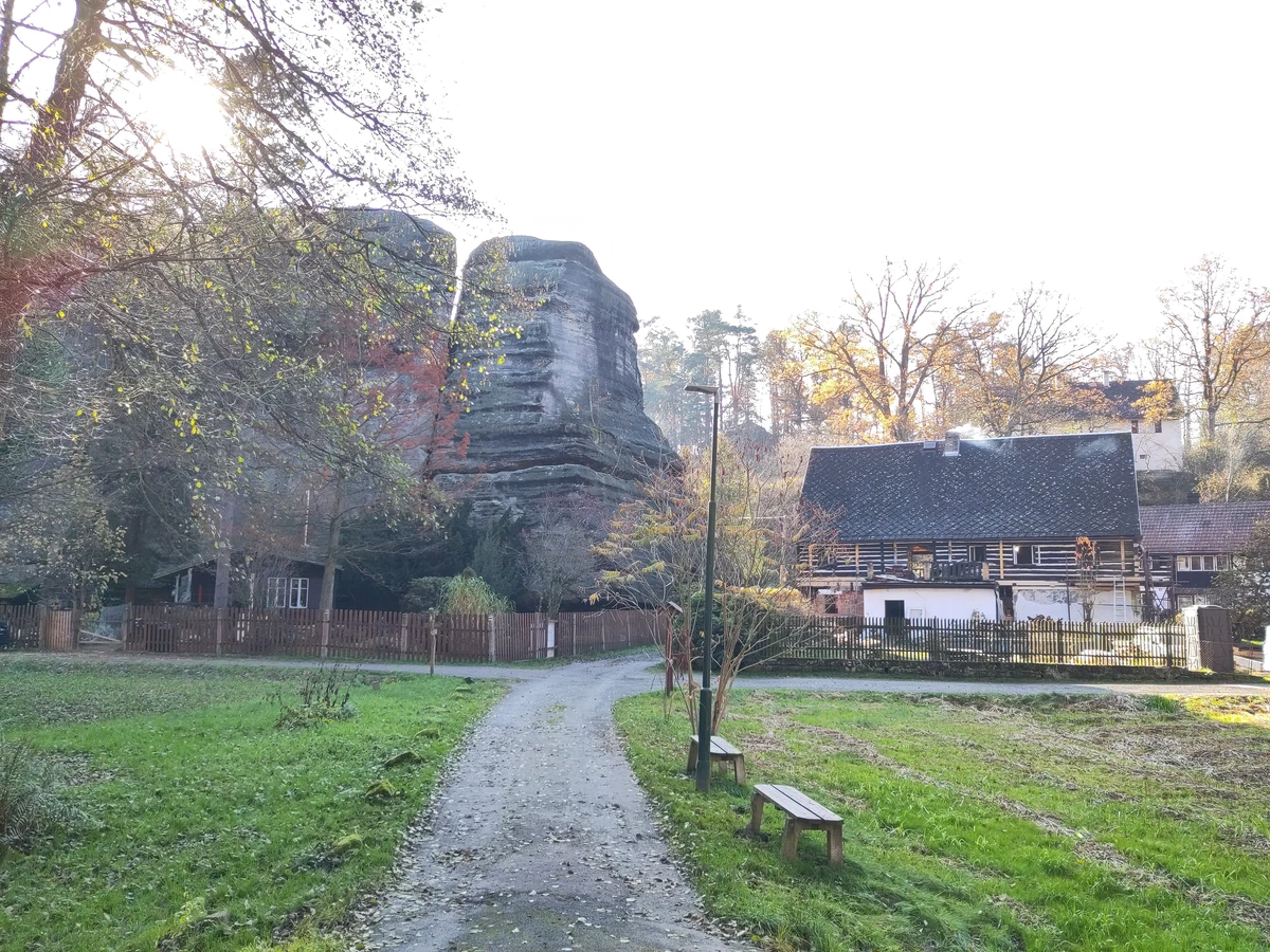 Fachwerkhäuser unterhalb eines Sandsteinfelsens, davor ein Weg durch die Wiese