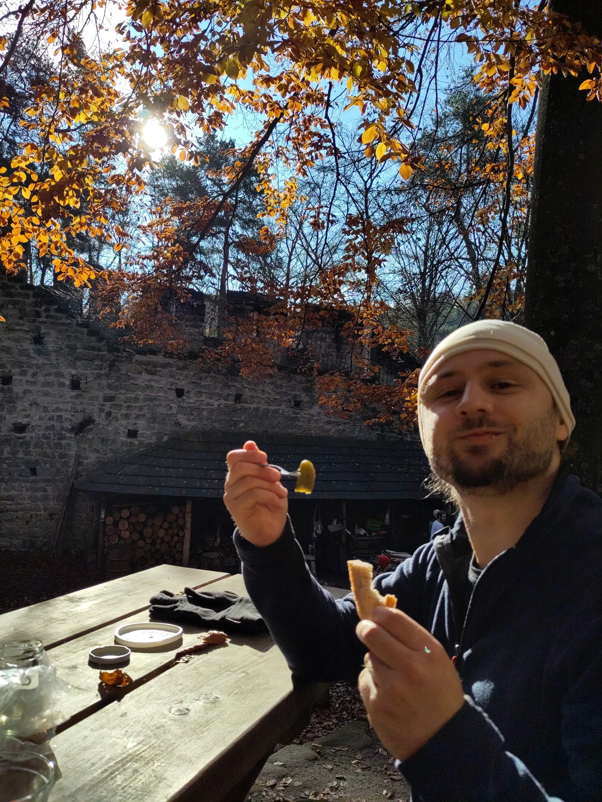 Ein Mann macht Brotzeit an einem Holztisch unter herbstlichen Buchen