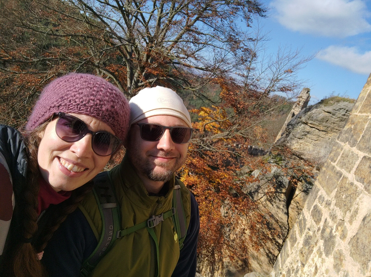 Selfie von uns beiden mit Mützen und Sonnenbrillen vor Burgmauer und Herbstlaub