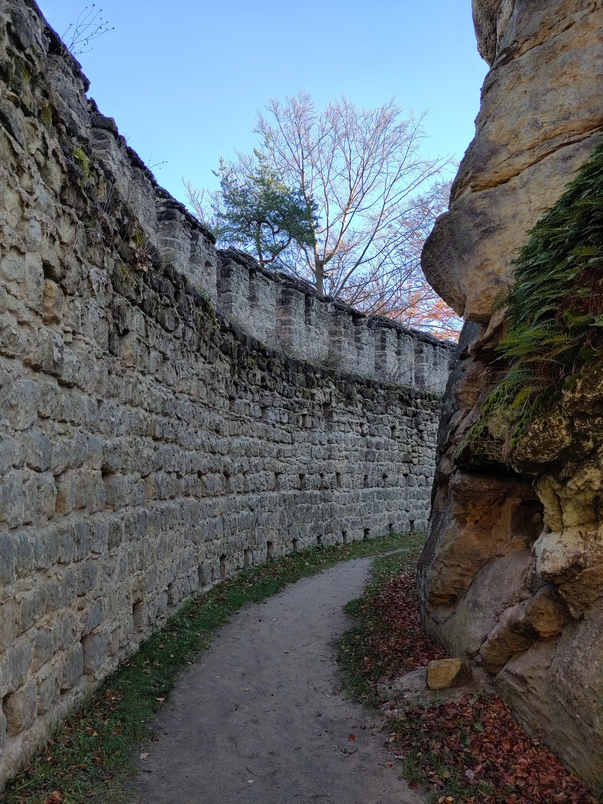 Weg zwischen einer hohen Steinmauer und einem Sandsteinfelsen
