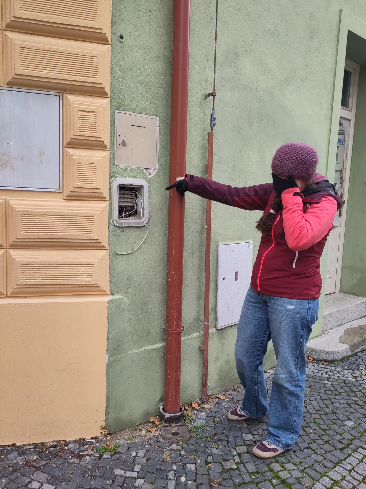 Eine Person hält sich die Hand vors Gesicht und zeigt auf eine improvisierte Installation an einer Hauswand