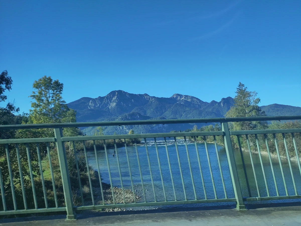 Blick von einer Brücke über einen Fluss auf einen Bergzug unter wolkenlosem Himmel