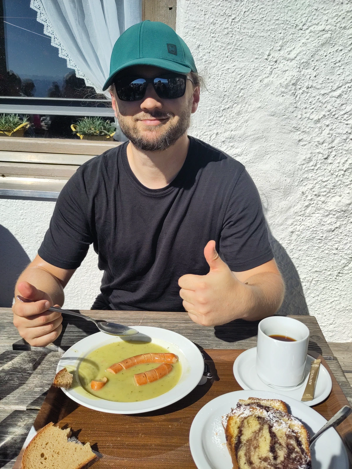 Ich sitze vor der Hütte in der Sonne, vor mir Erbsensuppe mit Würstl, Kuchen und Kaffee, Daumen nach oben