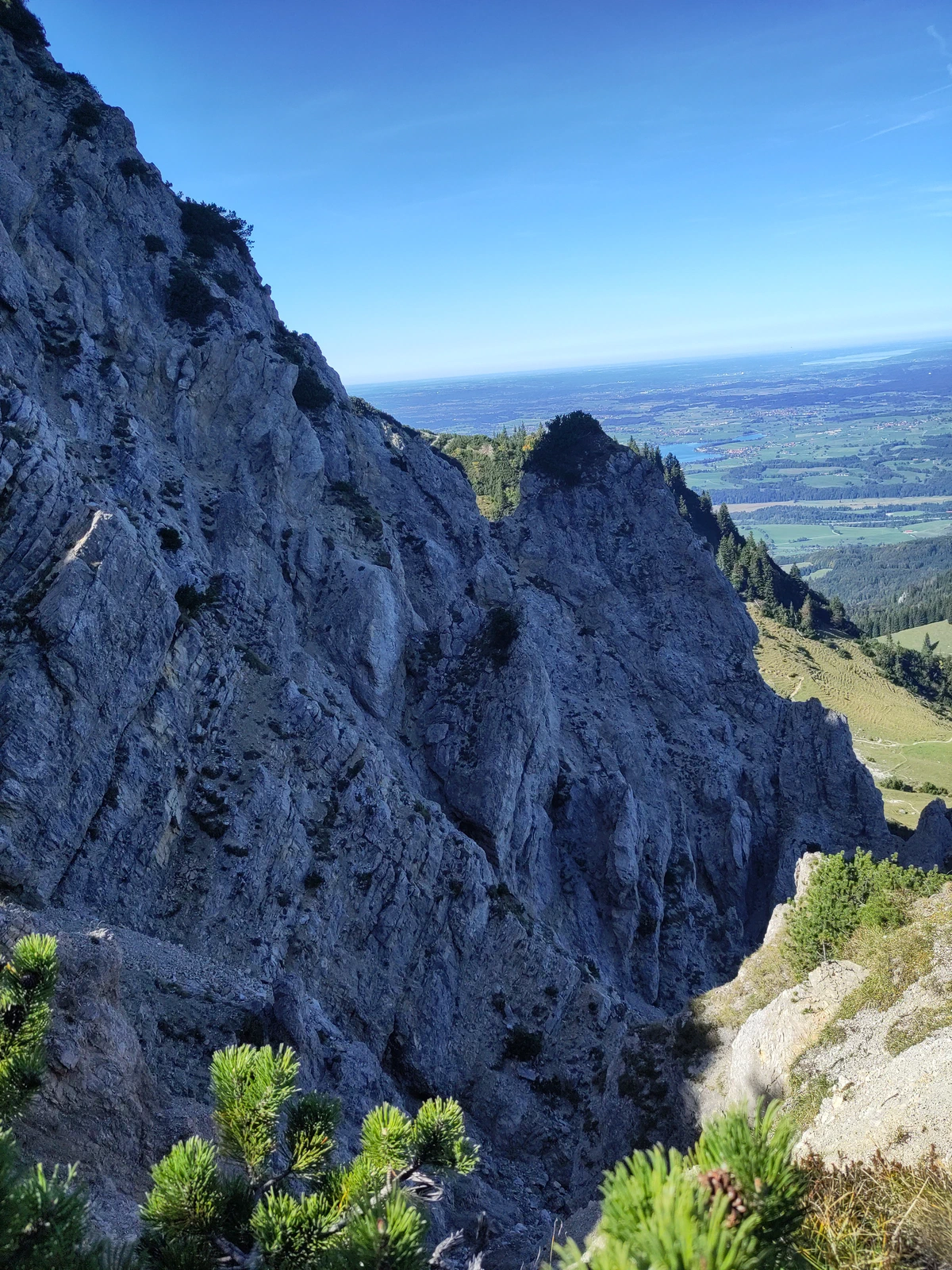 Steile Felswand am Grat, dahinter das flache Voralpenland