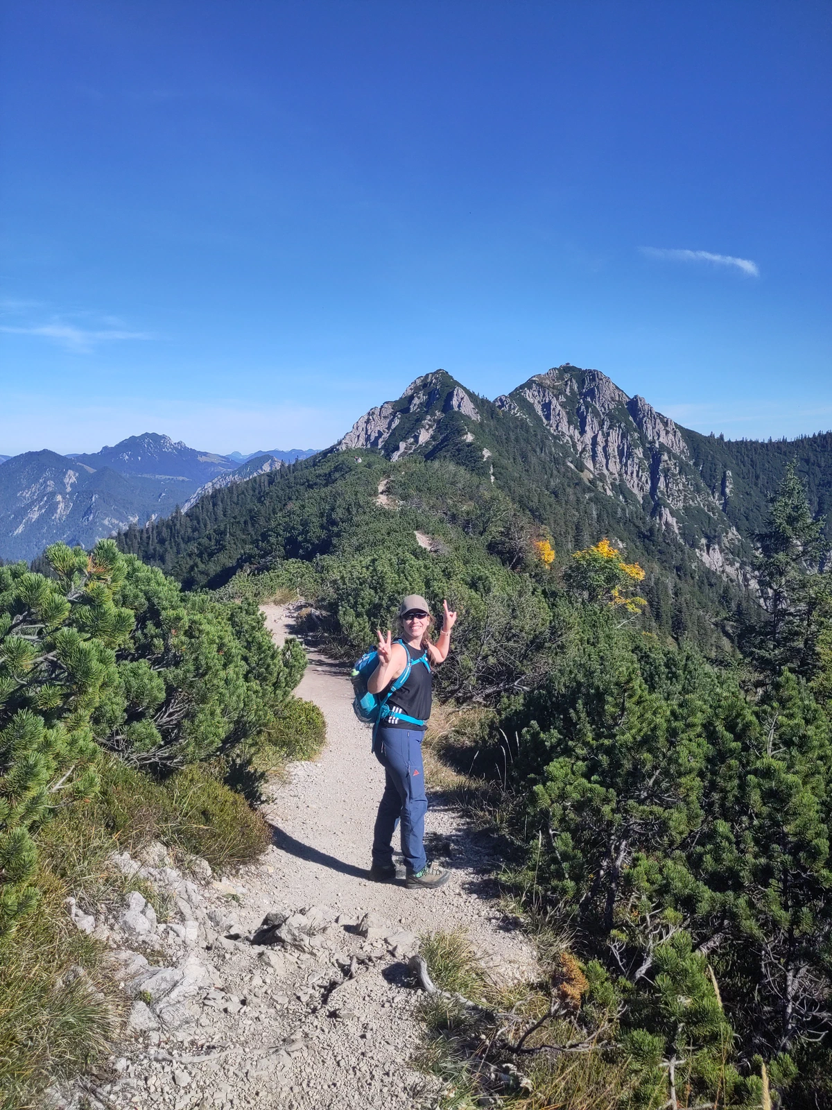 Karin steht auf dem schmalen Weg zwischen Latschenkiefern, hinter ihr der Grat