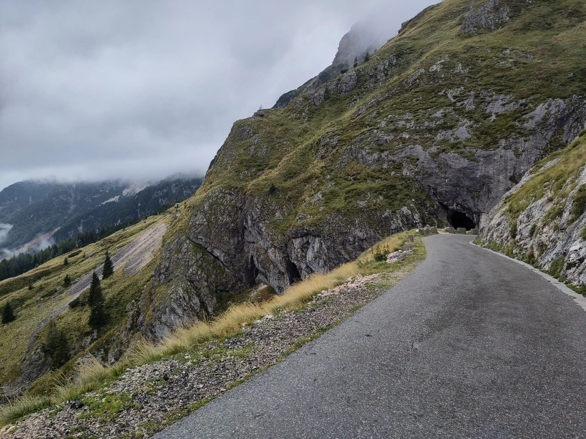 Schmale Passstraße am Mangart entlang steiler Grashänge unter tiefen Wolken