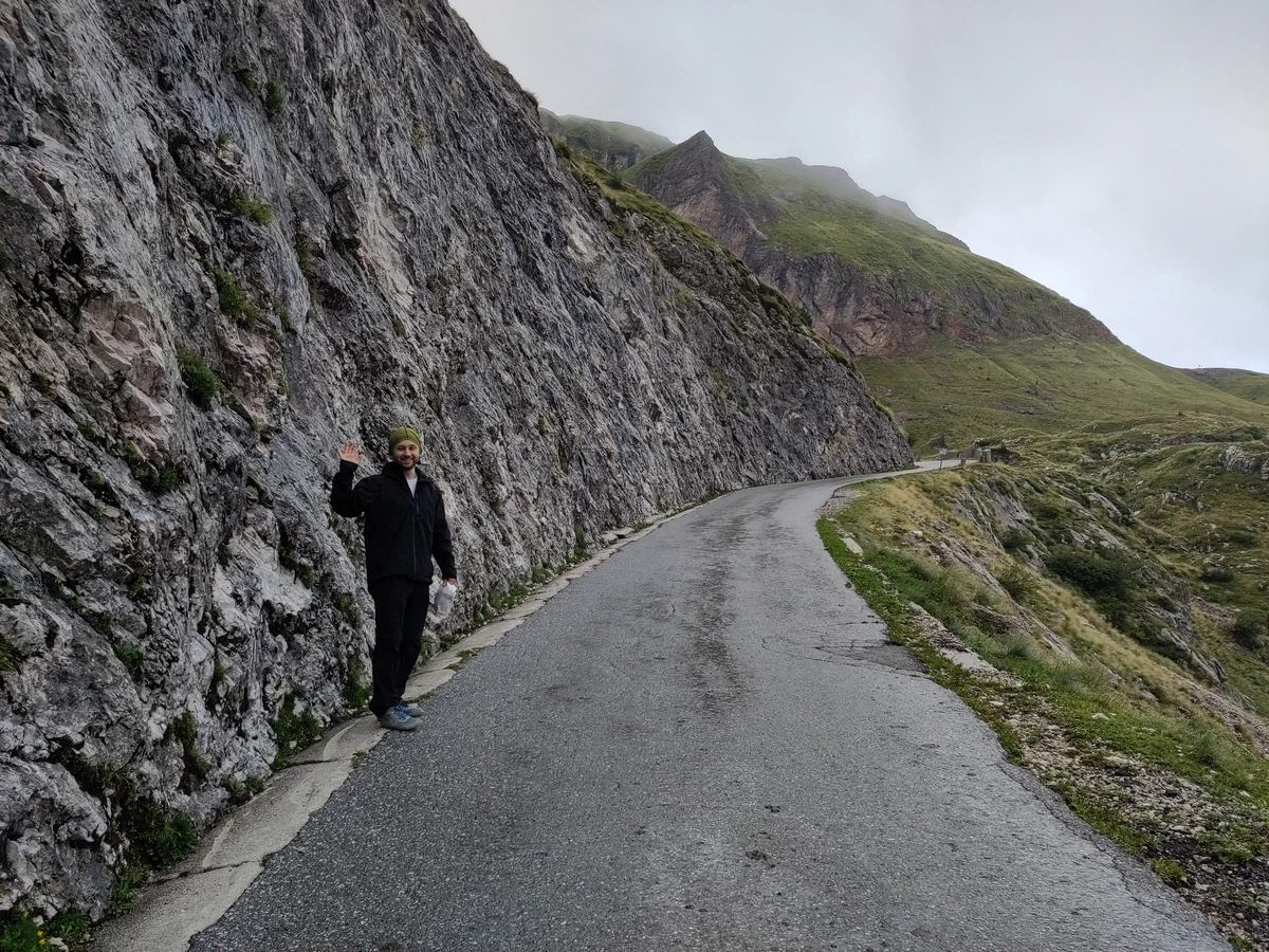 Eine Person winkt am Rand der schmalen Passstraße unter einer Felswand