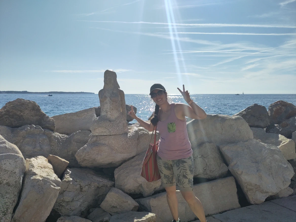 Eine Frau macht das Peace-Zeichen auf den Felsblöcken am Meer