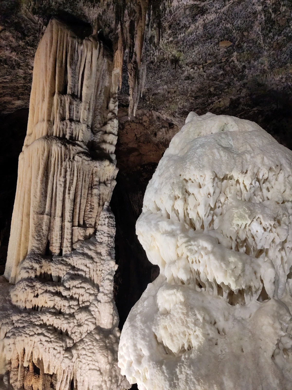 Heller, schneeweißer Stalagmit neben einer mächtigen Tropfsteinsäule