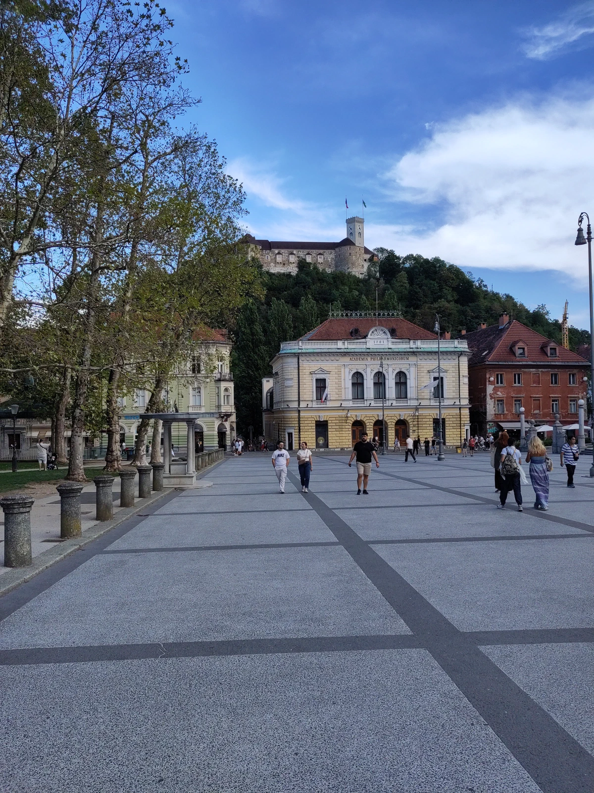 Weiter Platz in Ljubljana mit einem gelben Prachtbau, darüber die Burg auf dem Hügel