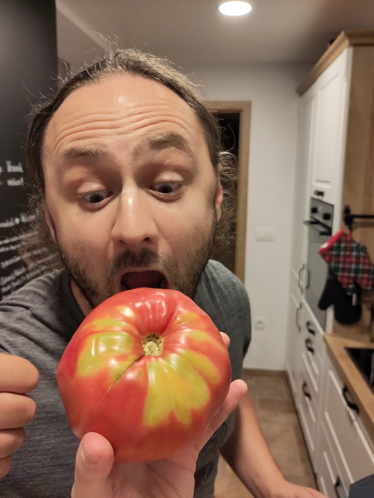 Ein Mann beißt mit aufgerissenen Augen in eine riesige Tomate