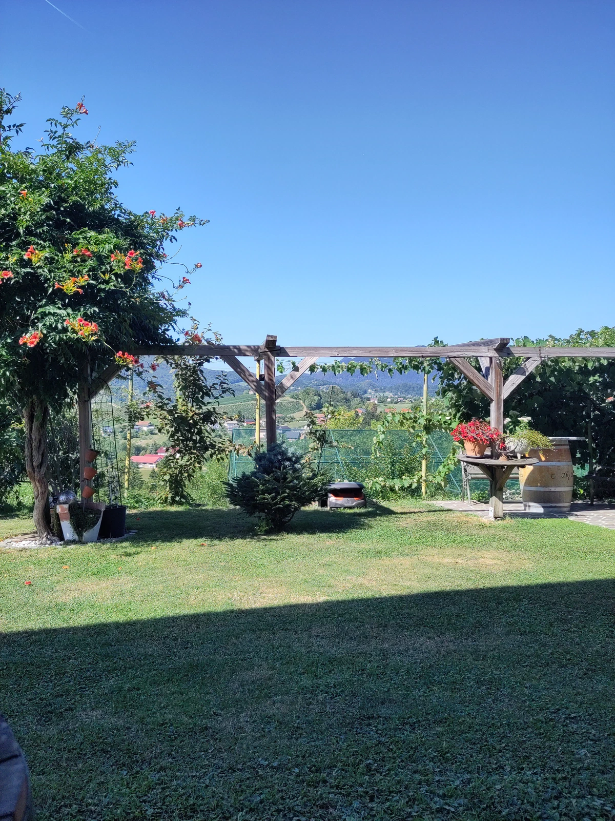 Garten mit Rasen, Pergola und Blick ins Tal unter wolkenlosem Himmel