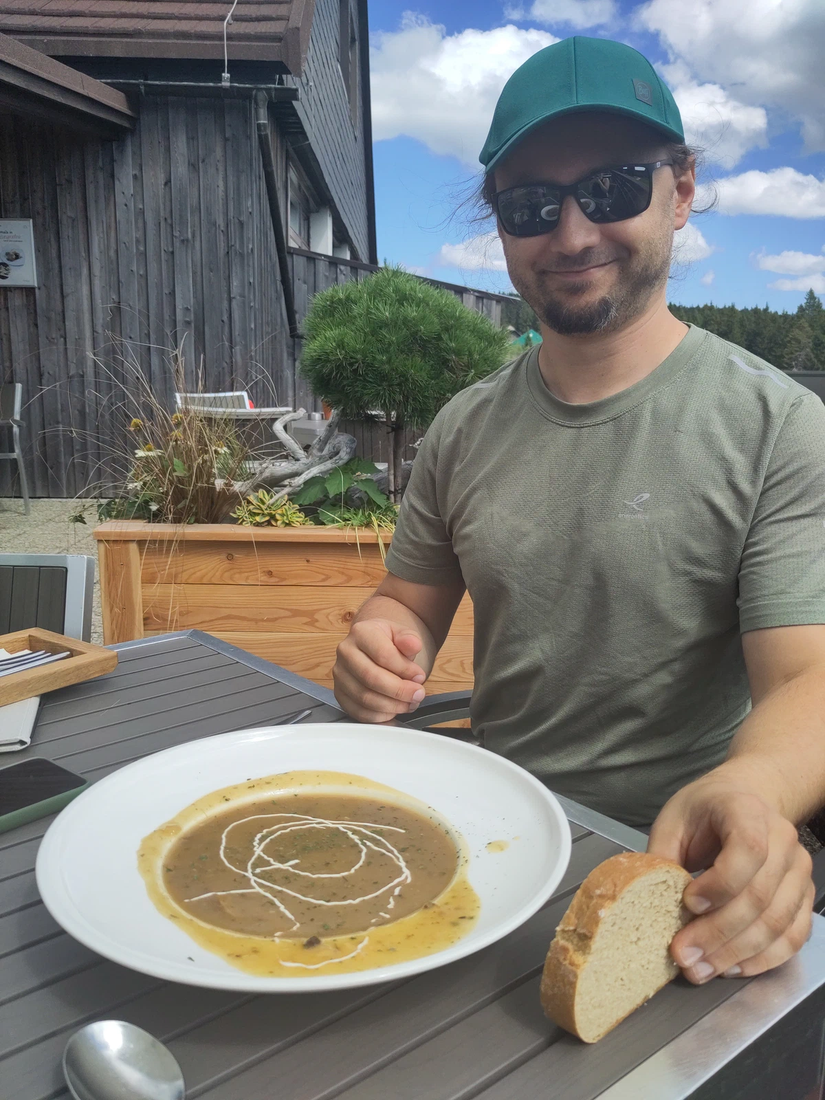 Ein Mann mit Kappe und Sonnenbrille sitzt vor einem Teller Schwammerlsuppe mit Brot