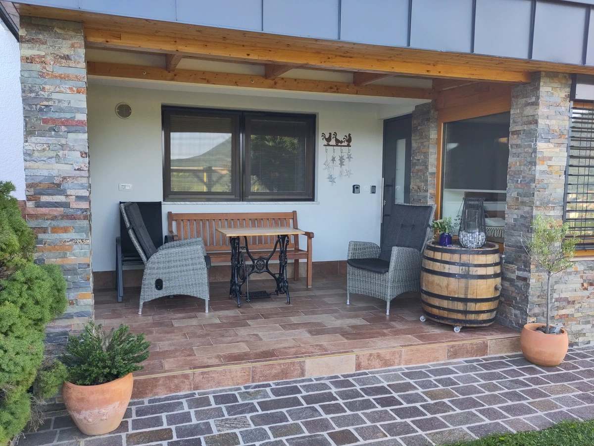 Überdachte Terrasse mit Sitzbank, Korbsesseln und einem Weinfass als Tisch